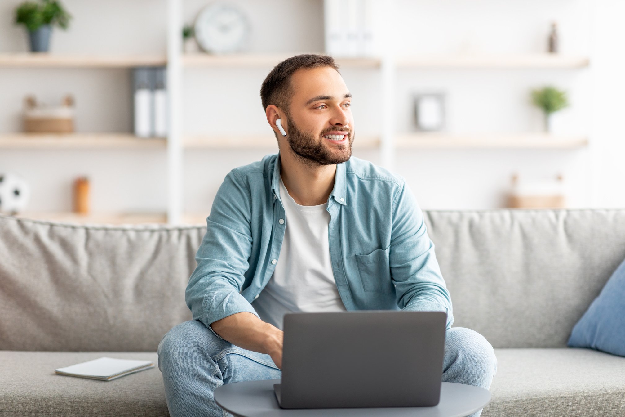 Smiling young man in earphones using laptop for online communication at home office